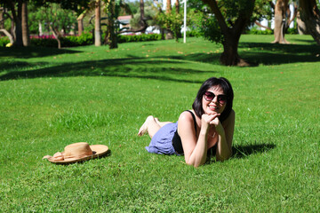 mature brunette sunglasses is relaxing on the green lush grass.