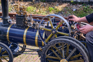 A detailed model steam engine with intricate accents shown with moving parts operated by hand outdoors in daylight. This image can be used for commercial purposes related to hobbies engineering