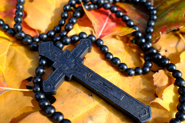 Traditional dark beaded rosary nestled on scattered autumn leaves, crucifix prominently displayed,...