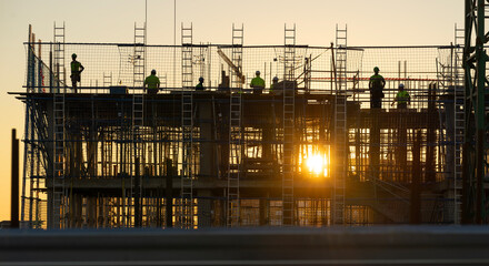 Backlit construction workers on a construction site at sunset.