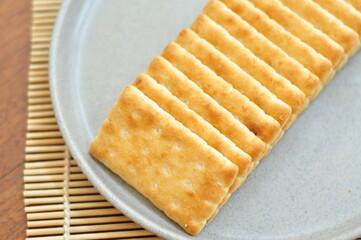 A close-up shot of several rectangular, light brown crackers stacked neatly on a speckled gray plate.