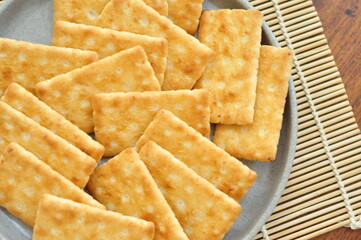 A close-up shot of several rectangular, light brown crackers stacked neatly on a speckled gray plate.