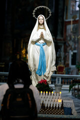 Basilica Santa Maria in Montesanto. Statue of Immaculate Virgin Mary, hands together in prayer, surrounded by flowers .