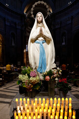 Basilica Santa Maria in Montesanto. Statue of Immaculate Virgin Mary, hands together in prayer, surrounded by flowers .