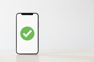 A phone with a green check mark on it. The phone is sitting on a table. The check mark indicates that the phone is functioning properly