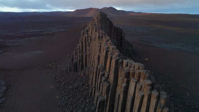 Sharp basalt formations stand across a barren volcanic plain, dark surfaces catching faint evening light.