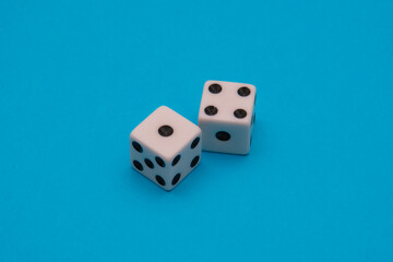 Two white plastic gaming dice displaying black pips rest on a bright, solid cyan blue background, emphasizing the concepts of probability and risk. Excellent for marketing concepts.