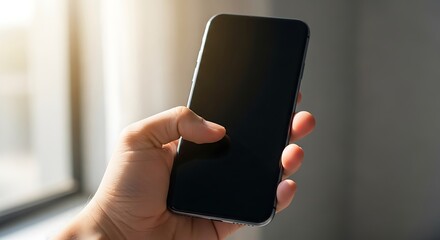 Hand holding a black smartphone with a blank screen in soft natural light mobile phone black screen
