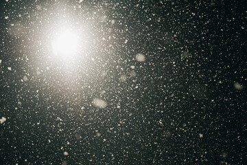 Countless snowflakes drift by at night, captured in midair and illuminated by a bright street lamp, creating a sparkling and atmospheric winter scene.