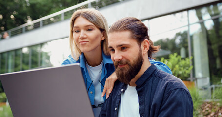 Close-up shot of two busy professionals man and woman using laptop outside, man giving an approving thumbs-up sign indicating successful work.