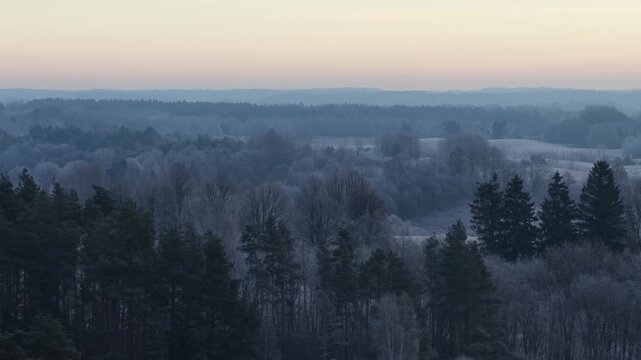 Panoramic view of frosted hills and forests under a warm sunrise sky, capturing the peaceful stillness of a rural winter landscape.