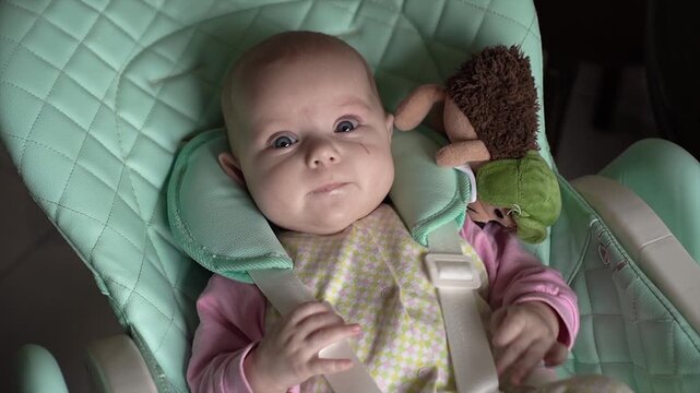 beautiful, happy, cute, surprised, excited little baby looks camera, blue eyes, child's chair kitchen, children's clothes. He amuses himself, shakes legs, arms, drools. Dimples cheeks scratch