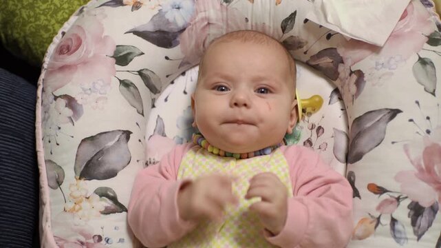 excited little baby, in a baby costume, puts his hands in his mouth, kicking his legs in a cozy cocoon with flower patterns in the bed close-up