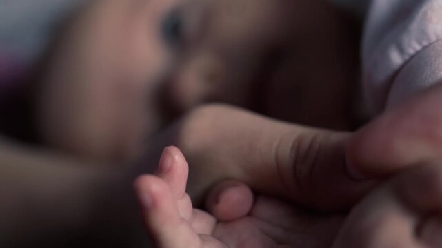 baby squeezes the hand, the thumb of mom, with a white manicure, with small fingers. Against the background of a child's face in blur. Soft skin