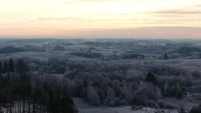 Panoramic view of frosted hills and forests under a warm sunrise sky, capturing the peaceful stillness of a rural winter landscape.