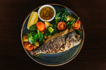 Grilled dorado fish served with vegetables and herbs with lemon on a plate on a wooden table