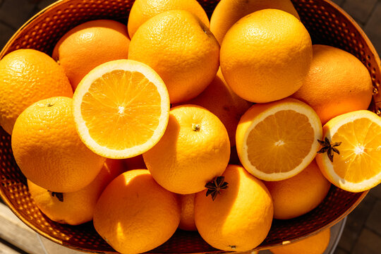 Many oranges in a vintage copper basket on a table in the sun.