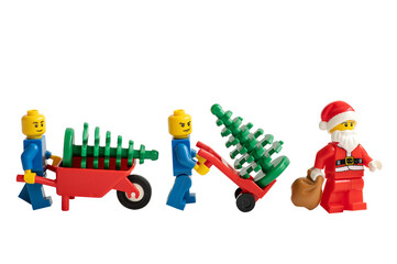 Obraz premium Santa Claus and miniature figurines with a wheelbarrow and Christmas trees on a white background