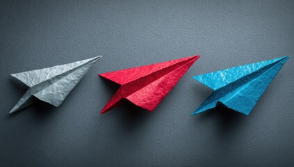Three origami paper airplanes of different colors on a gray background