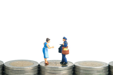 Miniature people toys conceptual photography. Cash on delivery and shipping cost service. Postman courier standing above money coin stack, isolated white background.