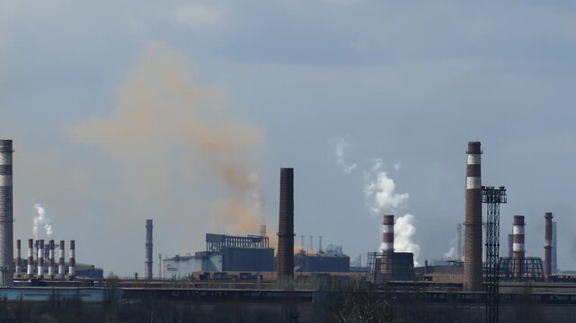Industrial landscape with huge chimneys releasing dense, chemically colored smoke into the atmosphere. Visible air pollution and toxic emissions from a metallurgical or steel factory.