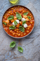 Mini potato gnocchi with tomato sauce and mozzarella, vertical shot on a beige and blue stone background, above view