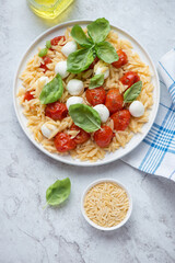 Plate of caprese pasta salad with orzo on a white stone background, vertical shot, view from above