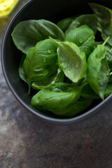 Close-up of a grey bowl with fresh green basil leaves, vertical shot, selective focus