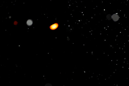 Bokeh effect of snowfall and lights. Abstract blurred background with snowflake in the night sky, White spots and dots in the dark. Snowy stormy weather, falling snow