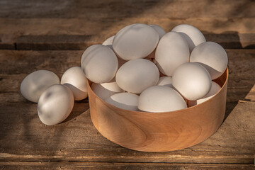 Chicken eggs in wooden bowl on grunge table in chicken coop, barn. Countryside outdoor setting in the backyard © TSViPhoto
