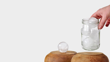 Glass jar with ice balls in hand, wooden pedestal podium. Ice freezing and melting processes. Cocktails, Frozen food concept, product promotion, cold water