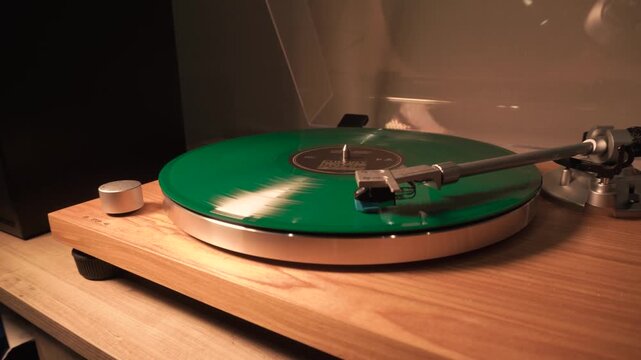bright new green music vinyl record plays smoothly on the device. the needle slides over it. close-up.yellow lamp light
