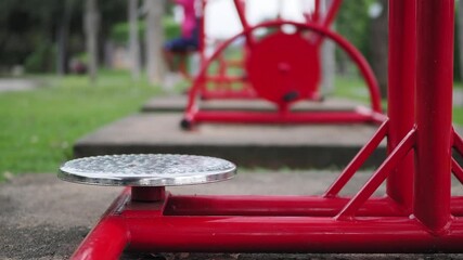  Man wearing black pants, a green shirt and green socks exercises outdoors with a red stainless steel exercise machine in a park.