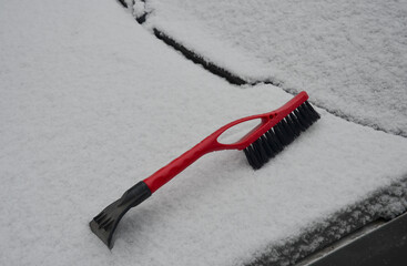 A brush for cleaning a car from snow lies on a car covered with snow.