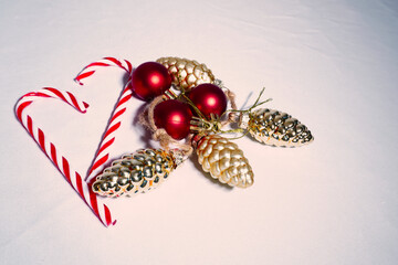 Two red and white candy canes forming a heart, clustered with red spherical and gold pinecone ornaments on a bright white background. Christmas love