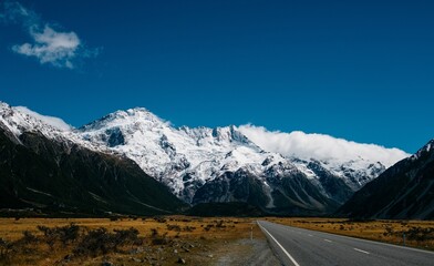 Scenic Road Leading Towards Majestic Snow-Capped Mountains Under a Clear Blue Sky