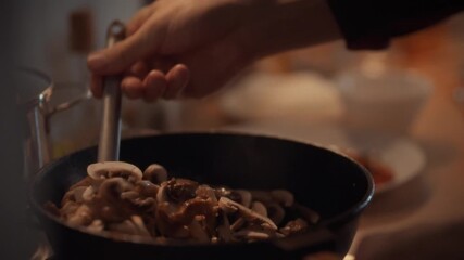 Champignon mushrooms are being stirred in a frying pan on a stove. The action takes place in a cozy kitchen, creating a delicious dish. The cook enjoys preparing this flavorful side - Powered by Adobe