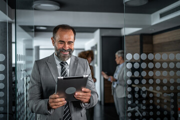 Smiling mature businessman holding digital tablet in modern office