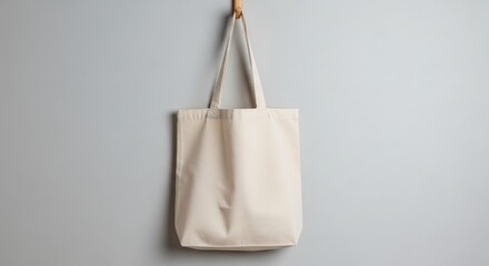 Elegant beige tote bag mockup hanging on a wooden hook against a light gray wall for design