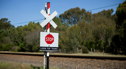 Railroad crossing sign with stop sign under a clear blue sky in rural countryside