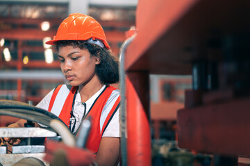 Professional Black African female factory engineer/worker/technician operate machinery in modern industrial plant. She wear safety helmet,vest show focus,skill in repair maintenance production process