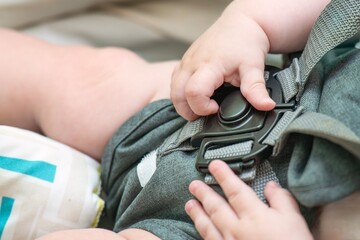 Small child's hands trying to open plastic safety lock on stroller harness straps