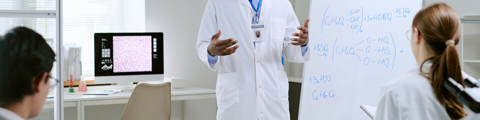 Website banner of Black man explaining medical concepts on whiteboard to woman and man in...