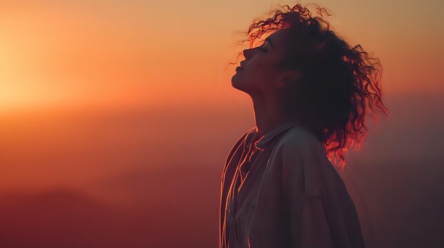 Silhouette of woman with curly hair against dramatic sunset sky, enjoying peaceful moment on mountain overlook. - Powered by Adobe