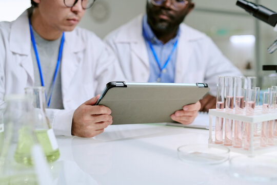 Young adult man and Black man wearing lab coats analyzing data on digital tablet in laboratory setting with glass test tubes - Powered by Adobe