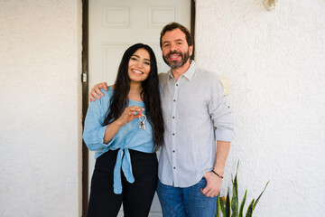 Smiling couple celebrating buying a new home. Woman holding house keys while man puts arm around her shoulders