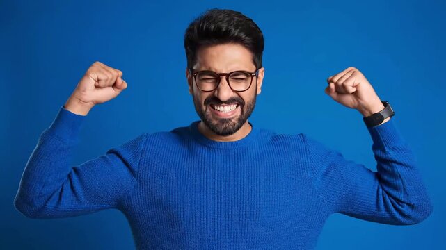 A man in a blue sweater and glasses flexes his biceps with a triumphant smile against a blue background.