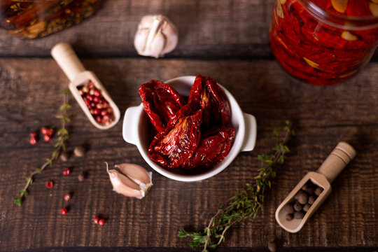 Sun-dried tomatoes in olive oil in a white bowl with pepper, garlic and thyme in a rustic style. Selective focus, close-up.