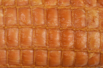 An extreme close-up, full-frame background of the shiny, golden-brown casing of a smoked meat roll, marked by a dense rectangular twine netting pattern