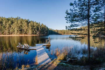 Serene lake view with wooden dock extending into calm waters, surrounded by lush green trees and tranquil nature, creating a peaceful outdoor retreat atmosphere
